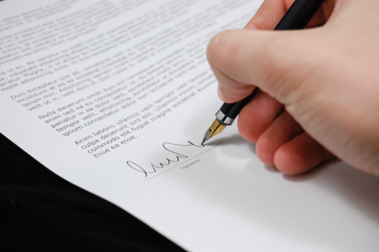 services-04 Close-up of a hand signing a legal document with a fountain pen, symbolizing signature and agreement.